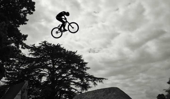 Someone on a mountain bike, high in the air, jumping over a ramp 