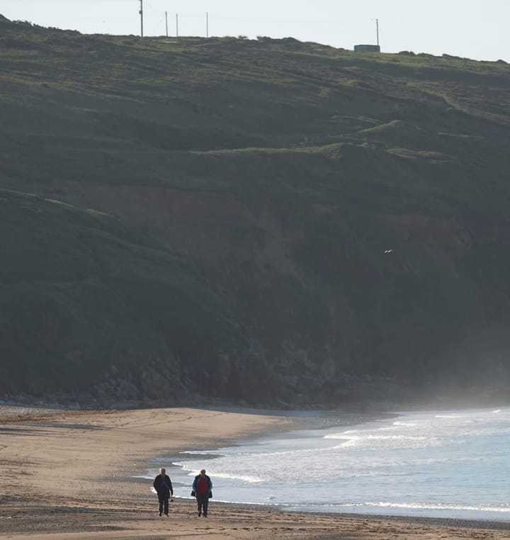 A couple stroll across Prah Sands beach in Cornwall