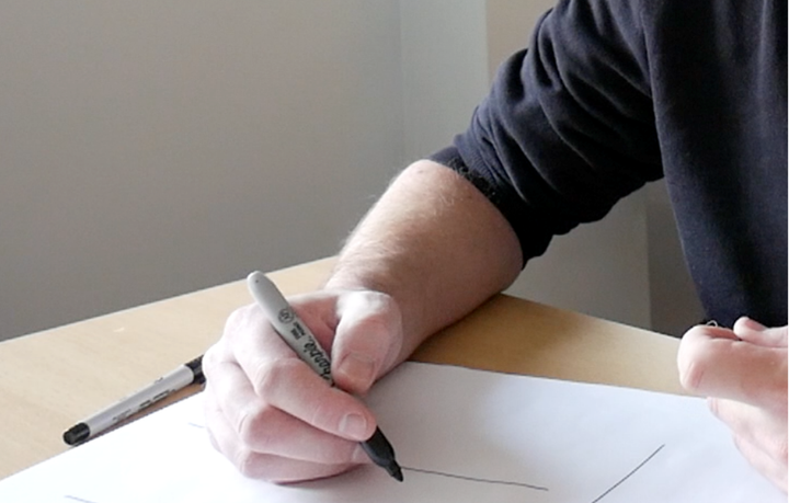 A photo of Rob Lambert writing on an A3 sheet of paper