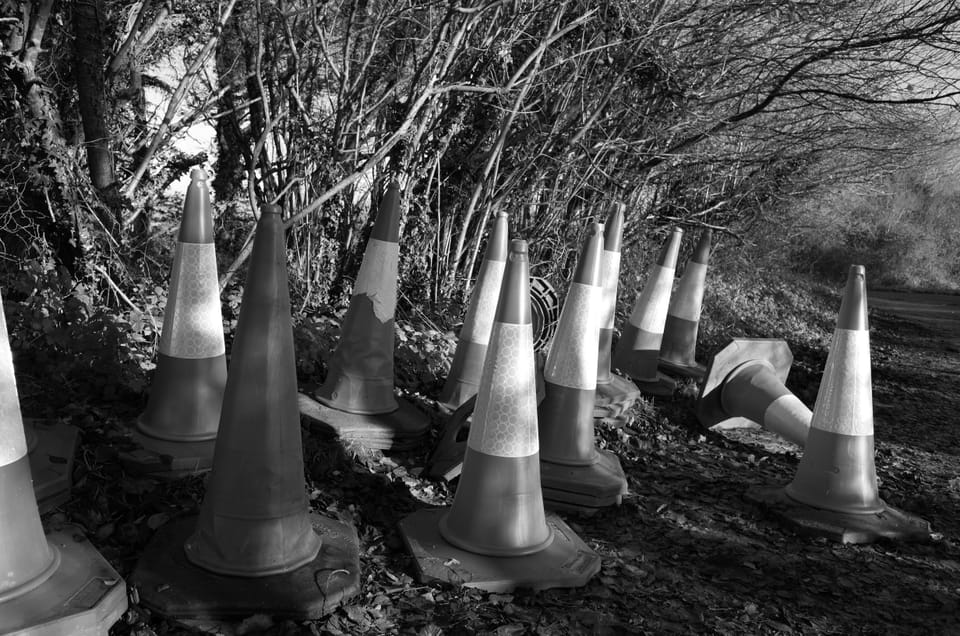 A photo of some traffic cones gathered at the side of the road by some trees